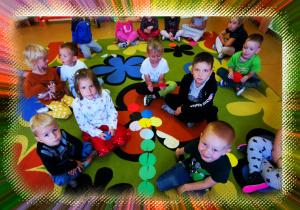 Grupa dzieci siedzi na dywanie. Przed nimi leży układanka z kolorowych kół.